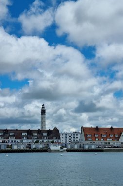 Calais, Fransa, 22 Haziran 2024: Belirgin bir deniz feneri ve kırmızı kiremit çatılı büyüleyici binaların yer aldığı pitoresk göl kenti. Parçalı bulutlu gökyüzü, sakin su sahnesine boyut katar. Seyahat terfisi, duvar sanatı veya selamlama için ideal.