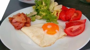 Besleyici bir başlangıç için kızarmış yumurta, pastırma, taze salata ve dilimlenmiş domatesli sağlıklı kahvaltı tabağı.