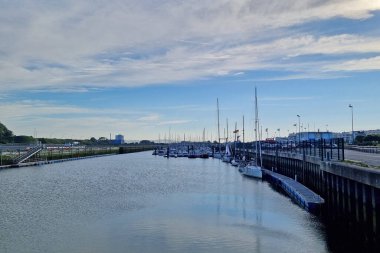 Calais, Fransa, 22 Haziran 2024: Birden fazla yelkenli limana yanaşmış, sakin sular ve engin, berrak bir gökyüzü ile çevrili bir marina manzarası. Huzurlu atmosfer ve resimli teknelerin yerleştirilmesi sakin bir deniz manzarası yaratıyor.