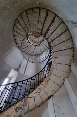 Terk edilmiş eski bir binanın içinde sarmal bir merdiven bulunan çarpıcı mimari fotoğraf. Çürüyen beton ve süslü metal tırabzanları yakalamak, bu görüntü kentsel bozulma ve karmaşık tasarım, sanatsal projeler veya mimari projeler için mükemmel 