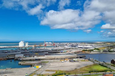 Calais, Fransa, 22 Haziran 2024: Uçsuz bucaksız okyanus ve mavi gökyüzünün bir zeminine karşı vinç ve konteynırlarla dolu yoğun bir kargo limanını gösteren çarpıcı bir hava manzarası. Bu dinamik kıyı sahnesinde sanayi yapıları ve depolama binaları öne çıkıyor..