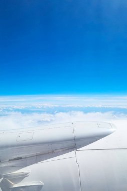 Arka planda parlak mavi bir gökyüzü bulunan tüylü bulutların üzerinde süzülen bir uçak kanadının yüksek çözünürlüklü görüntüsü, seyahat, havacılık ve macera temalı baskı tasarımları veya çevrimiçi içerik için mükemmel..