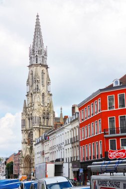 Lille, France, June 23, 2024: Eglise saint-maurice, showcasing stunning gothic architecture, stands prominently in lille, france. the towering spire and intricate details of the church contrast with the vibrant red buildings and bustling urban street clipart