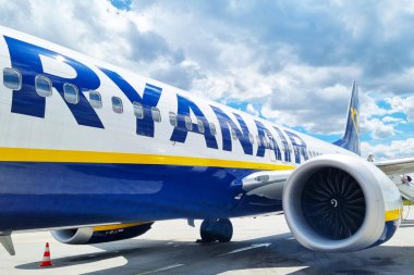 Wroclaw, Polonya, 18 Haziran 2024: Ryanair yolcu jeti bulutlu açık mavi bir gökyüzünün altında bir havaalanı pistinde konumlandırıldı. Uçak tarafı ve motoru belirgin bir şekilde görünür, ikonik logosunu sergiliyor. Havaalanının küçük bir bölümü ve bir uçak pisti.