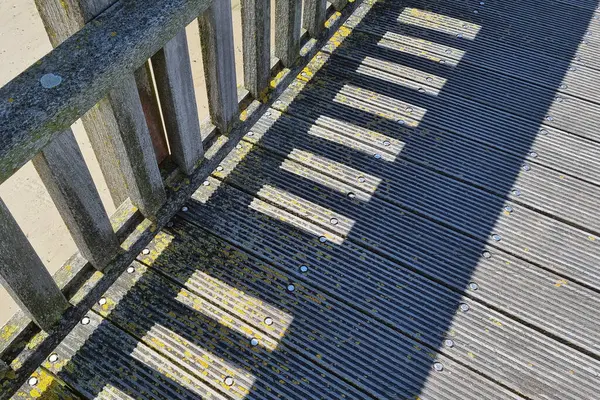 stock image Wooden pier with vibrant shadow patterns cast by the planks and railings. the sunlight creates a striking, geometric effect, emphasizing the textures and weathered look of the wood. ideal for coastal and maritime-themed design projects.