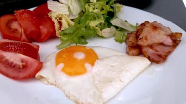 Besleyici bir kahvaltı tabağı. İçinde mükemmel pişmiş güneşli bir yumurta, taze yapraklı salata, sulu domates dilimleri ve çıtır pastırma var. Sağlıklı yeme alışkanlıklarını, sabah yemeklerini veya