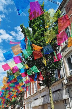 Lille, Fransa, 23 Haziran 2024: Gökyüzünde parlak mavi bir gökyüzüne karşı asılı sayısız renkli uçurtmalarla süslenmiş canlı bir şehir caddesi. Sahne şenlik, neşe ve açık hava kutlamalarını simgeliyor. Festival promosyonları, etkinlik posterleri ya da mevsim için mükemmel.