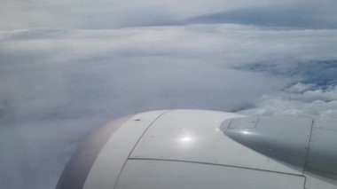 Bir uçak penceresinden çarpıcı bir hava görüntüsü, uçsuz bucaksız kabarık beyaz bulutlar denizi üzerinde sakin mavi bir gökyüzüne karşı eşsiz bir perspektif sağlar. Seyahat, havacılık ve atmosfer temalı tasarım veya yayınlar için ideal.