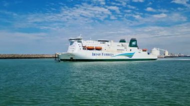 Calais, Fransa, 22 Haziran 2024: Büyük bir İrlanda feribotu berrak, mavi bir gökyüzü altında hafif bulutlarla kaplı sakin kıyı sularında yol alır. Geminin çevresi sarılmış durumda.