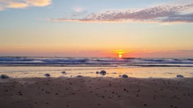Canlı bir günbatımı sahnesi. Huzurlu bir okyanus sahili. Hafif dalgalar kıyıya vuruyor. yumuşak bulutlar rengarenk gökyüzüne yayılır, ve deniz köpüğü kumlu sahili süsler, huzur verir ve