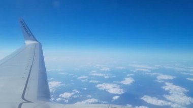 Wroclaw, Polonya, 18 Haziran 2024: Bir uçak penceresinden çarpıcı manzara, uçağın kanadını, açık mavi gökyüzünü ve aşağıdaki dağınık bulutları gösteriyor. Seyahat temaları, tanıtım materyalleri ya da hava yolculuğunun güzelliğini resmetmek için ideal.
