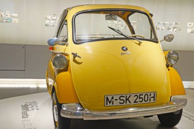 Münih, Almanya, 25 Ağustos 2024: Müzede sergilenen klasik sarı 1955 bmw isetta microcar arka planda tarihi fotoğrafların bulunduğu cam kasalar. Mikro arabanın kompakt formu ve tek kapı gibi eşsiz tasarım özellikleri promindir.