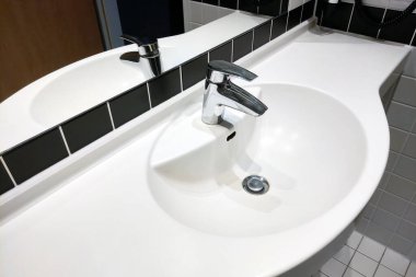 Pürüzsüz kıvrımları olan minimalist beyaz bir lavabo, parlak krom bir musluk ve temiz, beyaz bir tezgah. Siyah-beyaz seramik zemin sıçraması uzayın modern estetiğini geliştirir..