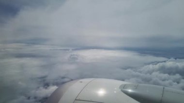 Bir uçak penceresinden gelen hava perspektifi içinden süzülen yumuşak ışık filtreli geniş beyaz bulutlar sergiliyor. Uçağın motoru ve kanadı görülebilir durumda. Seyahat ve keşif duygusu katıyor.