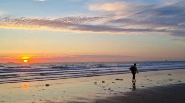Huzurlu bir sahilde görkemli bir gün batımı, dalgaların kıyıya vurduğu bir yer. Yalnız bir sörfçü, canlı gökyüzüne karşı siluetlenmiş, sakin akşam manzarasına biraz macera katıyor. ideal