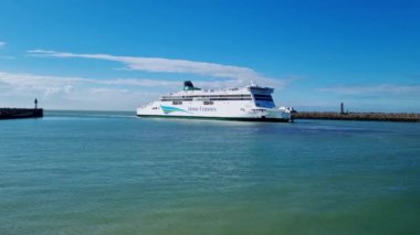 Calais, Fransa, 22 Haziran 2024: Büyük, beyaz bir feribot kıyıya yakın sakin, yeşil-mavi sularda yol alır. Sahne, parlak, açık mavi bir gökyüzünün arka planında geçiyor.