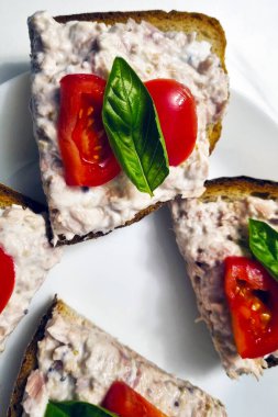 Taze vişneli domates ve tam tahıllı tost üzerine fesleğen yapraklı ton balıklı sandviç. Sunum sağlıklı bir yemek veya aperatif için canlı ve iştah açıcı bir seçenek sunar..