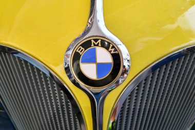 Münih, Almanya, 25 Ağustos 2024: Canlı, sarı klasik bir araba ızgarasına karşı klasik bir BMW amblemi. Görüntü, klasik otomotiv engisinin ustalığını ve zarafetini vurgulayarak ikonik rozeti ve şık tasarım unsurlarını vurguluyor.