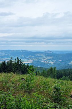 Canlı yeşilliklerin ve bulutlu bir gökyüzünün altında yuvarlanan tepelerin yer aldığı yemyeşil bir dağ manzarasının huzurlu bir görüntüsü. Kırsal kesimin huzuru, doğa meraklıları için ideal..