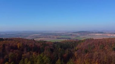 Manzaralı hava manzarası, canlı orman tepeleri, açık kırsal alanlar ve açık mavi gökyüzü ile geniş bir sonbahar manzarasını gösteriyor. Doğa sahneleri, seyahat promosyonları ve mevsimlik tasarımlar için ideal.