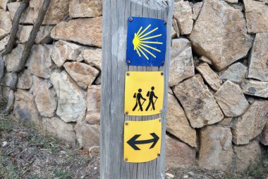 Trail markers for camino de santiago featuring iconic yellow symbols, guiding hikers along a stone wall path. these indicators provide direction and assurance for travelers on this famous pilgrimage route. clipart