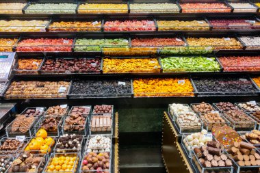 Barselona, İspanya, 1 Ekim 2024: Renkli şeker ve kurumuş meyvelerden oluşan geniş bir koleksiyonun sergilendiği canlı bir süpermarket koridoru, birden fazla sıra ve kompartımanda düzenli bir şekilde düzenlenmiştir. Çok çeşitli tatlı ikramları keşfetmek için mükemmel..
