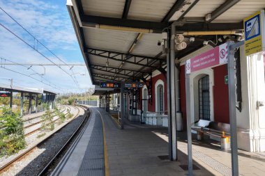 Lloret de Mar, İspanya, 3 Ekim 2024: Çağdaş bir tren istasyonu, açık mavi gökyüzünün altında altyapının parlak tasarımını vurgulayan boş bir platforma sahiptir. Olay yerinde izler, kapalı bekleme alanları ve bilgilendirme levhası yer alıyor.