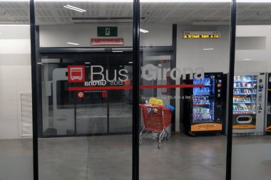 Girona, İspanya, 3 Ekim 2024: Girona 'daki otobüs terminali girişinde belirgin tabela ve cam kapılar bulunmaktadır. İçeride, bir alışveriş arabası eşliğinde bir otomat alanı görülebilir durumda. Sahnenin işlevsel tasarımı toplu taşıma verimliliğini yansıtıyor.