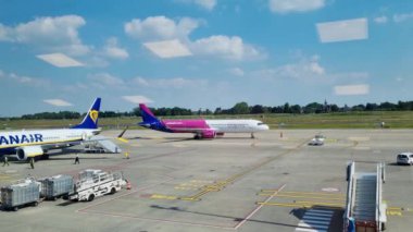 Wroclaw, Polonya, 18 Haziran 2024: Meşgul bir havaalanında iki ticari uçak park halindedir. Havaalanı personeli ve yer ekipmanları, hareketli faaliyet ve ulaşım