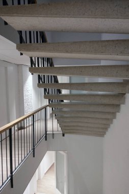 Parlak, açık bir iç mekâna kusursuz bir şekilde entegre edilmiş, beton basamakları ve siyah parmaklıkları olan gösterişli, minimalist bir tasarıma sahip modern merdiven. Çağdaş mimari estetiği ve mekansal verimliliği vurguluyor.