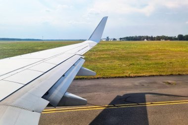 Bir uçak penceresinden podyumun arka planına ve geniş kırlara karşı kanadı gösteren bir görüntü. Açık bir günün sakin atmosferi, uçuş sırasında teknoloji ve doğayı harmanlıyor..