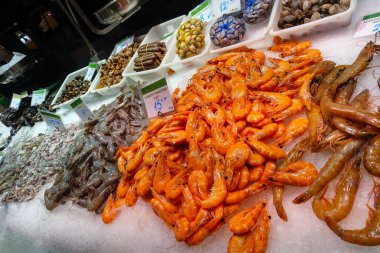 Barselona, İspanya, 1 Ekim 2024: Canlı bir deniz ürünleri pazarı, buz, tazelik ve mutfak çeşitliliğinde sergilenen turuncu karides, istiridye ve çeşitli kabuklu deniz ürünleri de dahil olmak üzere çeşitli taze deniz ürünleri sergiliyor.