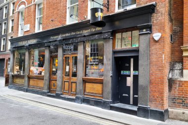 Londra, Birleşik Krallık, 30 Haziran 2024: Kırsal tuğla cephesi ve geleneksel tabelanın yer aldığı tarihi İngiliz barı. Ilık ışıklandırılmış pencereler, samimi bir iç mekan, somut şehir cazibesi ve klasik bar kültürünün davetkar atmosferi hakkında ipuçları veriyor..