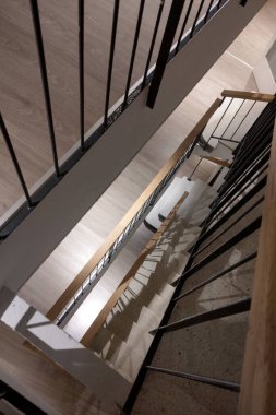 Modern mimari tasarım unsurlarının sergilendiği, parlak metal korkuluklar ve ahşap basamakları birleştiren çağdaş bir merdivenin yukarıdan aşağı bakışı. İç tasarım ve inşaat kavramları için ideal.