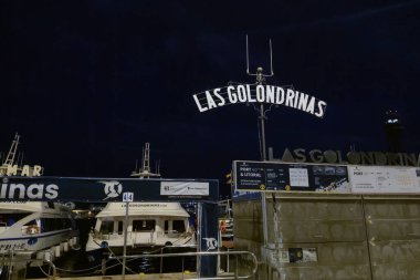 Barselona, İspanya, 1 Ekim 2024: Gece görüşü Las golondrinas limanının tekneli ve ışıklı tabelalı hali. Sakin rıhtım sahnesi temiz gökyüzünü ve liman bölgesinin sakin atmosferini suni aydınlatma altında sergiliyor..
