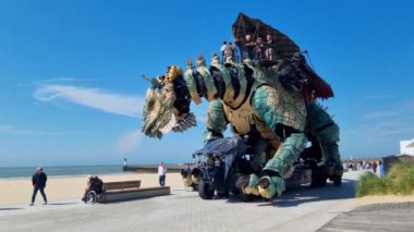 Calais, Fransa, 22 Haziran 2024: Büyük bir mekanik ejderha, karmaşık tasarımı ve canlı benzeri hareketiyle aileleri memnun etmek için sahil kenarında geziniyor. Çocuklar ve yetişkinler korku içinde izliyorlar.