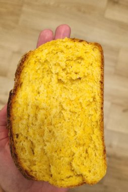 Bir avuç içinde duran altın mısır ekmeği diliminin yakın plan görüntüsü, parçalanmış dokusu ve zengin rengi. Kırsal ahşap arka plan mısır ekmeğinin ev yapımı ve rahatlatıcı hissini vurguluyor..