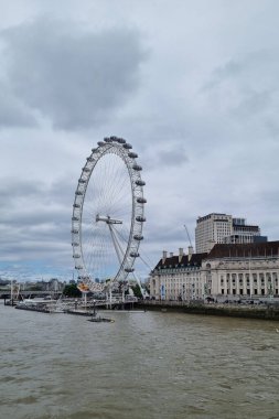 Londra, Birleşik Krallık, 30 Haziran 2024: Iconic London Eye Thames nehrinin yanında yer alan bulutlu bir gökyüzüne karşı duruyor. Bu dev dönme dolap şehrin çarpıcı panoramik manzarasını sunuyor, mimarını yakalamaları için turistleri ve fotoğrafçıları çekiyor.