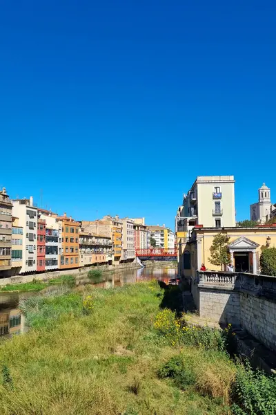 Girona, İspanya, 5 Ekim 2024: canlı mavi gökyüzü altında renkli tarihi binaların olduğu Riverside sahnesi. Mimari, nehir kıyısı yakınlarında geleneksel ve modern tarzların karışımının yer aldığı mekanın cazibesini vurguluyor..