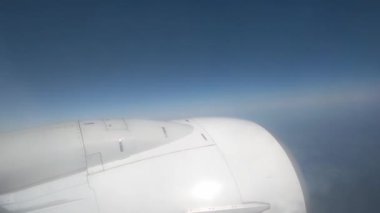 Açık mavi gökyüzüne karşı kanat ve motoru gösteren bir uçak penceresinden sakin bir manzara. Seyahat, havacılık ve macera temaları, özgürlük ve keşif hissi sunar.