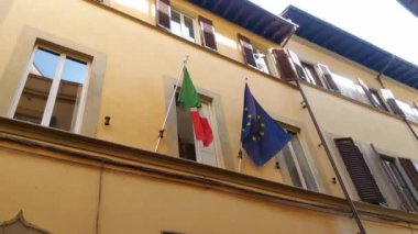 Floransa, İtalya, 10 Mayıs 2024: Avrupa Birliği ve İtalya bayrakları tarihi bir binanın ön cephesinde asılı duruyor. Mimaride klasik pencere panjurları ve sıcacık sarı bir dış görünüş var.