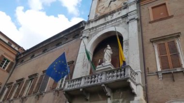 Modena, İtalya, 14 Mayıs 2024: Bir saat kulesinin yer aldığı zarif bir Avrupa binasının mimari detayları. Ulusal ve eu bayrakları yapıyı süslüyor, tarihi önemi ve kültürü simgeliyor. a