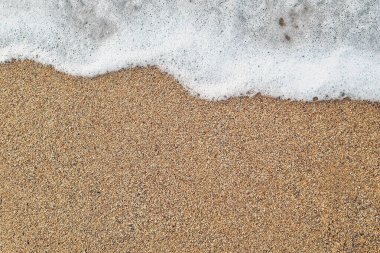 Yumuşak bir okyanus dalgasının yakından görüntüsü yumuşak bir kumlu plajın üzerinde yavaşça süzülüyor. köpüklü su ve kum tanelerinin zıt dokuları sakin ve sakin bir sahil manzarası yaratır..