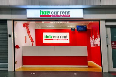 Milan, İtalya, 2 Aralık 2024: Canlı kırmızı ve beyaz tasarım unsurları barındıran araba kiralama ofisi. Sergiler arasında markalaşma, şık bir sayaç, dijital ekran ve İtalya temalı duvar sanatı yer alıyor. Seyahat ve ulaşım görsel temalar için uygun.