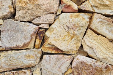 Kırsal taştan bir duvarın detaylı bir yakın plan görüntüsü. Çeşitli dokuma taşları içeren toprak tonlarda. Mimari projeler, tasarım arkaplanları veya doğal temalı görsel kompozisyonlar için ideal.