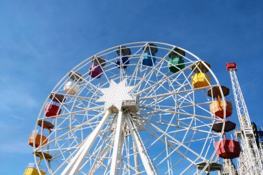 Parlak bir dönme dolap, açık mavi gökyüzüne karşı dimdik ayakta duruyor. Renkli kulübeler sergiliyor. Bu klasik lunapark gezisi eğlenceli yaz maceralarını ve festival alanlarını simgeliyor. Promosyon malzemeleri ve seyahat broşürleri için mükemmel..