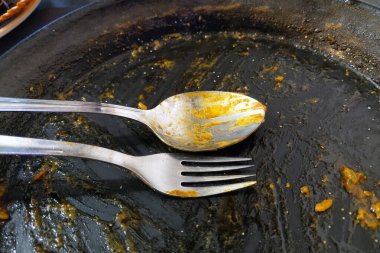 Pişirdikten sonra yağlı bir tencerede duran kirli çatal ve kaşık doyurucu bir yemeğin sonucunu gözler önüne seriyor. Bu resim ev yemeği pişirme, yemek hazırlama ve kaçınılmaz temizlik sürecini çağrıştırıyor..