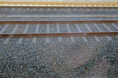 Paralel demiryolu rayları çakıl yatağı üzerinde uzanır, ulaşım, altyapı ve yolculuk kavramını vurgular. Kompozisyon, demiryolu seyahatinin simetri ve perspektifini vurguluyor, hareket ve macera hissi uyandırıyor.