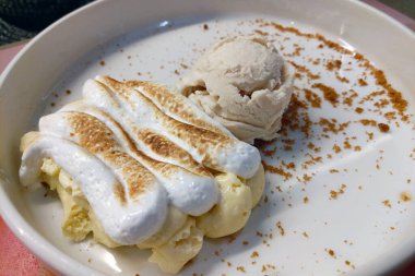 Mükemmel kızarmış kremalı muzlu pudingin olduğu lezzetli bir tatlı, yanında da bir kepçe kremalı dondurma. Kaplama, ilave doku için bir parça kurabiye kırıntısı içeriyor..