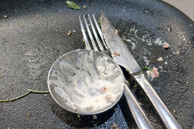 Çatal ve bıçak boş bir tabakta yemek lekeleri ve tatminkar bir yemek olduğunu gösteren boş bir sos tabağı ile dinleniyor. Bitki parçaları biraz renk ve detay ekler. Lezzetli bir yemek ve zevk olduğunu gösterir..
